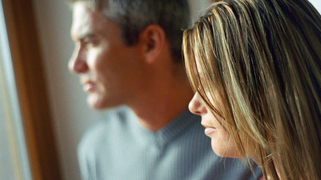 En mann og en kvinne står side om side innendørs og ser ut av et vindu. Fokus er på kvinnen i forgrunnen, mens mannen i bakgrunnen fremstår som litt uskarp.