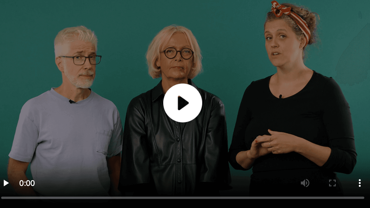 Tre personer står foran en blågrønn bakgrunn. En eldre mann med briller og lys skjorte står til venstre, en eldre kvinne med blondt hår og briller står i midten, og en yngre kvinne i svart står til høyre og snakker.